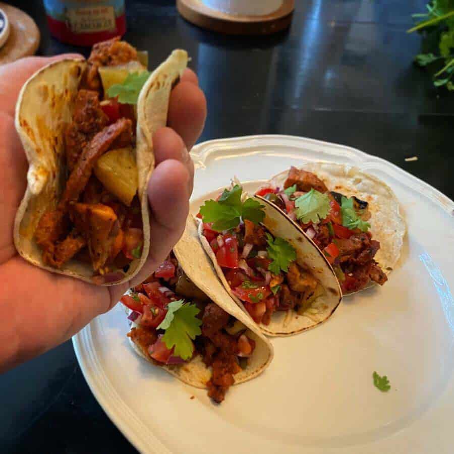 pehmeitä Tacos al pastor -tacoja kädessä ja lautasella
